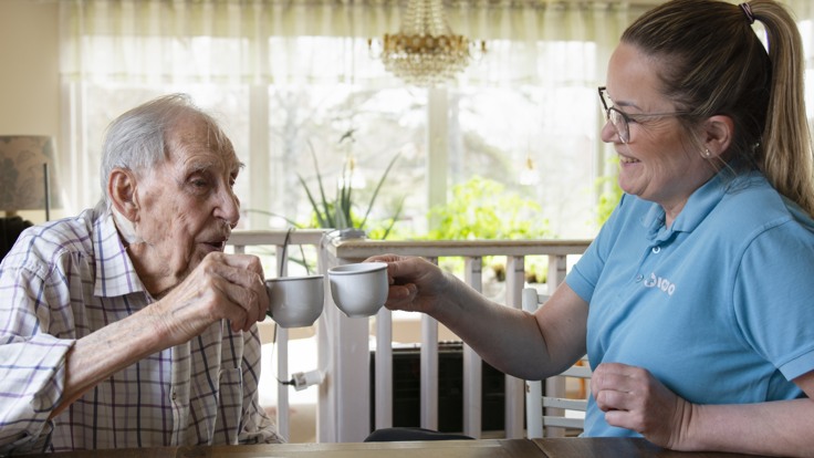 Äldre man och hemtjänstpersonal skålar med kaffekoppar